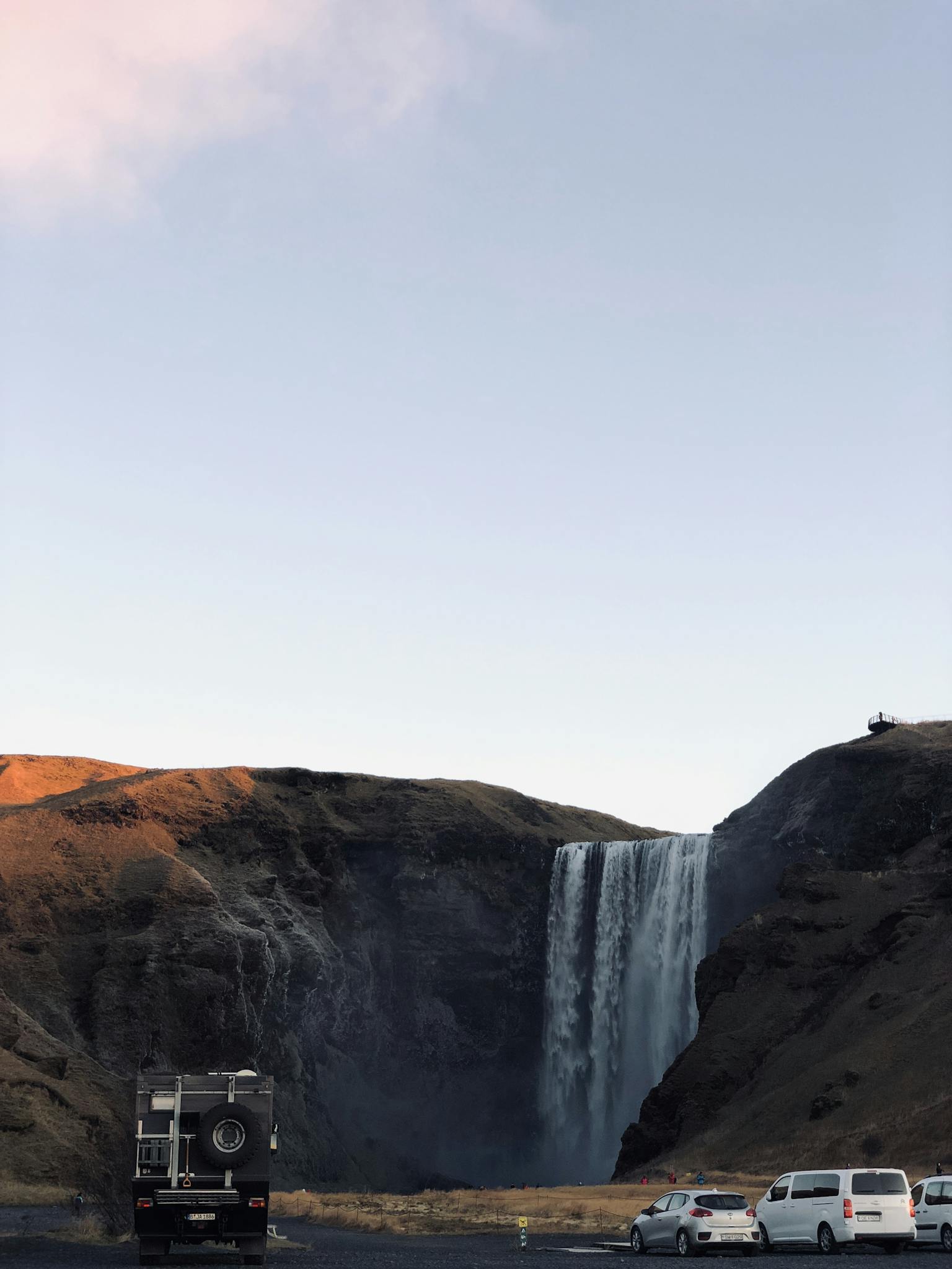 A stunning view of Skógafoss waterfall surrounded by campers under a clear evening sky in Vik, Iceland.