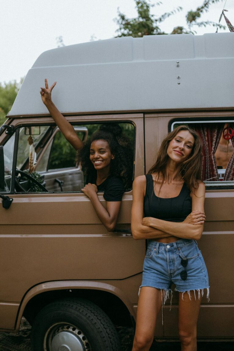 Two women enjoying a fun road trip, posing beside a vintage camper van outdoors.